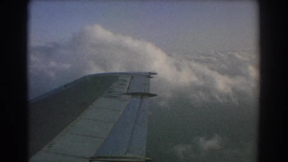 1967 8mm home-movie view from an airplane window near Perth, showing the wing passing above dense clouds.