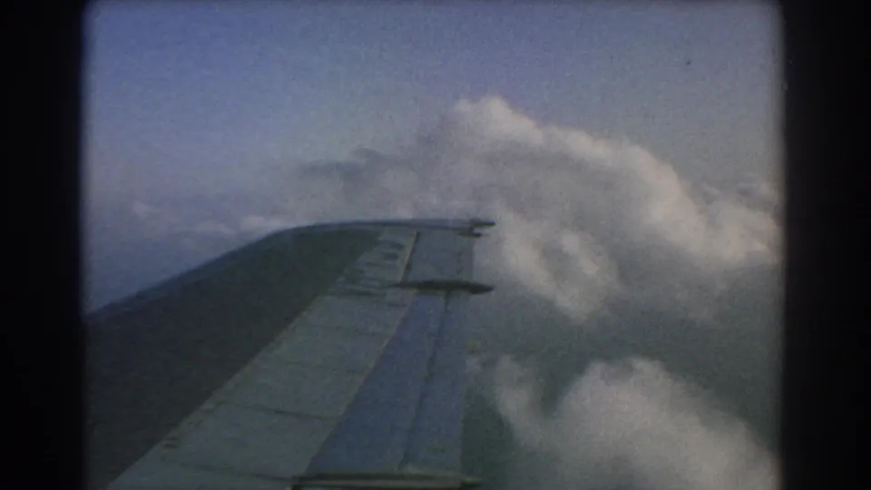 Home-movie frame from a 1967 flight near Perth, showing the airplane wing and bright cloud forms below.