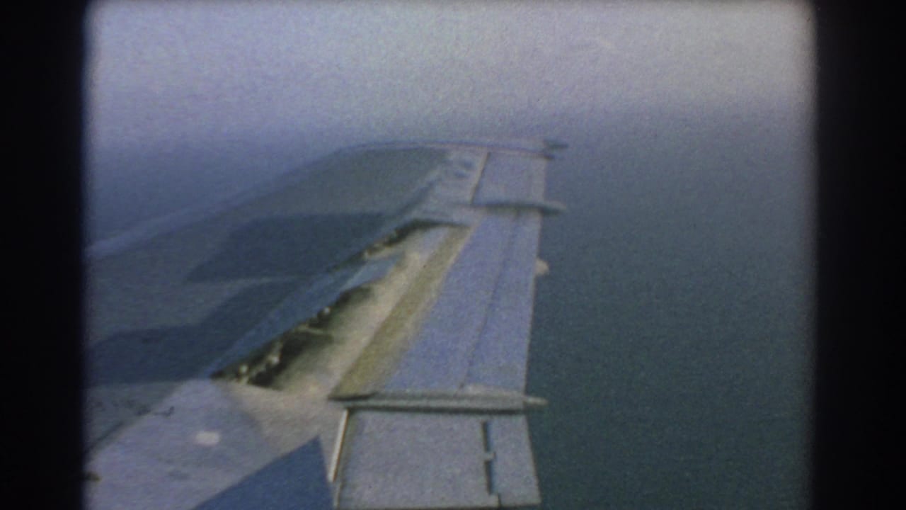 1967 8mm travel footage near Perth, Australia, showing an aircraft wing with extended slats above hazy blue water from a passenger-window viewpoint.