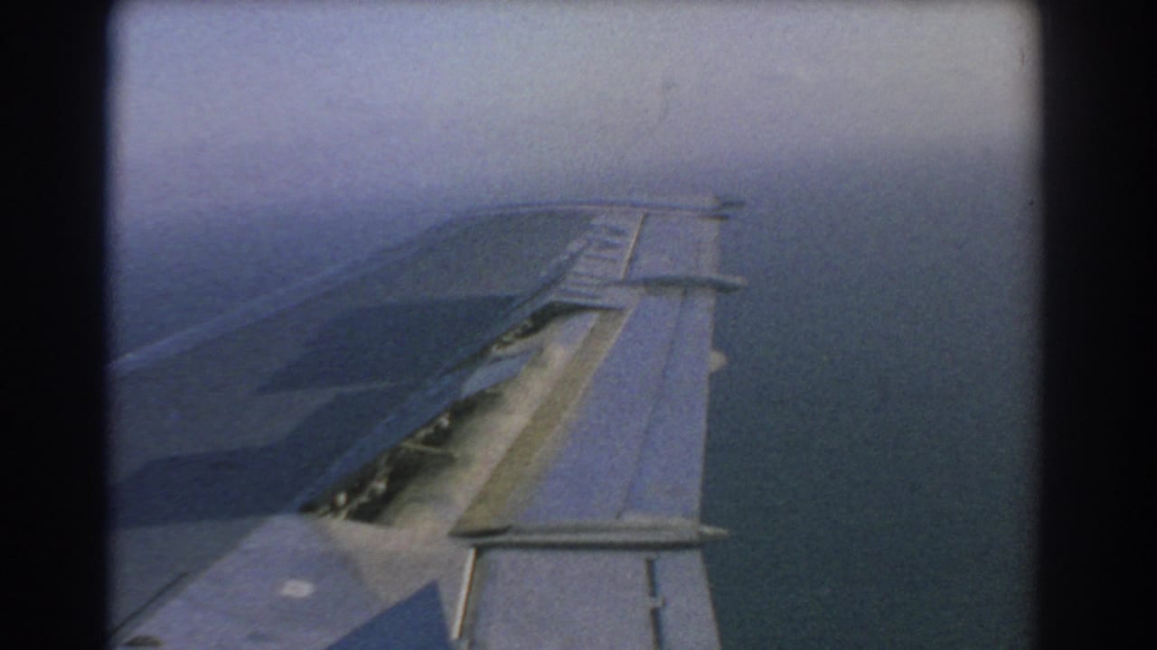 Aircraft wing and raised slat surfaces visible against hazy sky and water.