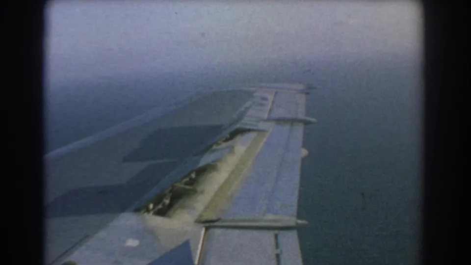 1967 home-movie frame showing a close view of an aircraft wing with open slats or flap surfaces above blue water, filmed from inside the airplane near Perth, Australia.