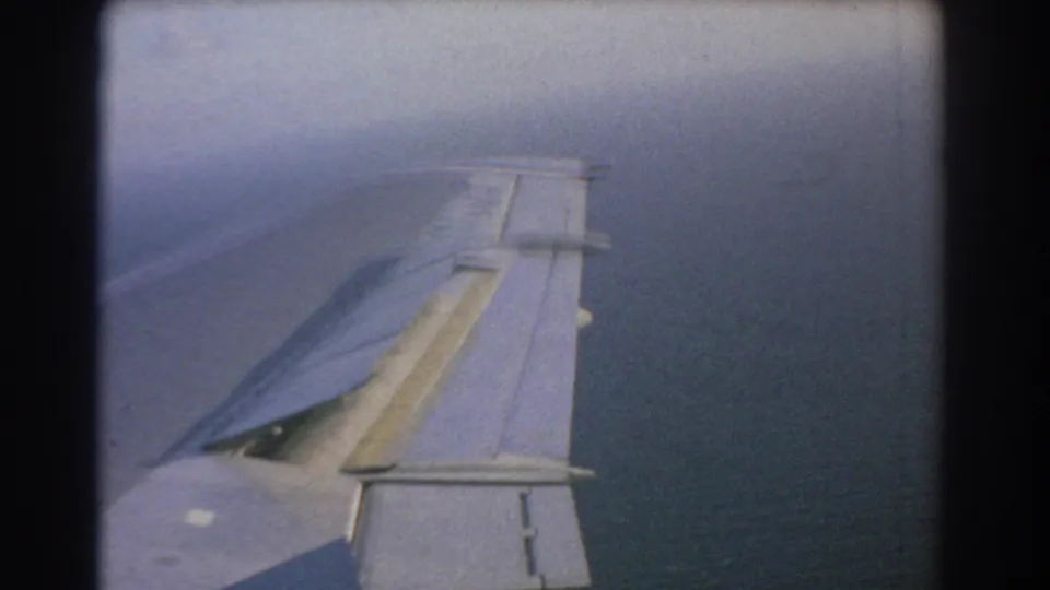 Final frame of the 1967 8mm Perth travel clip showing the aircraft wing from a passenger-window angle, with open water and hazy sky in the background.