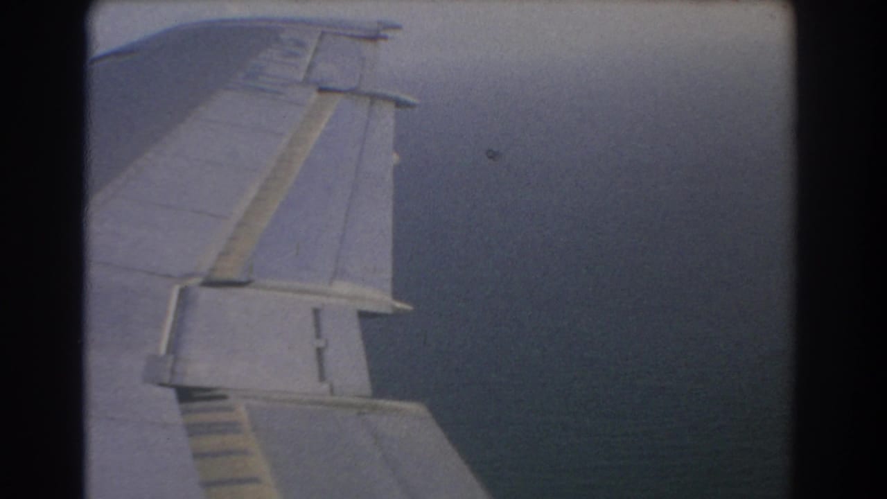 Airplane wing seen through a window against blue-gray cloud cover.