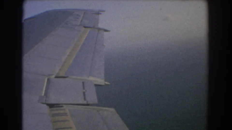 8mm in-flight view from a passenger window, showing the airplane wing against thick cloud cover near Perth in 1967.