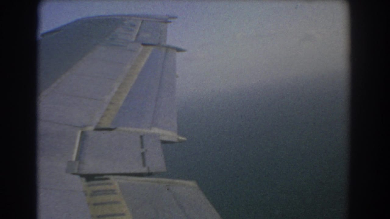 Airplane wing seen through a window over blue-gray sea and hazy sky.