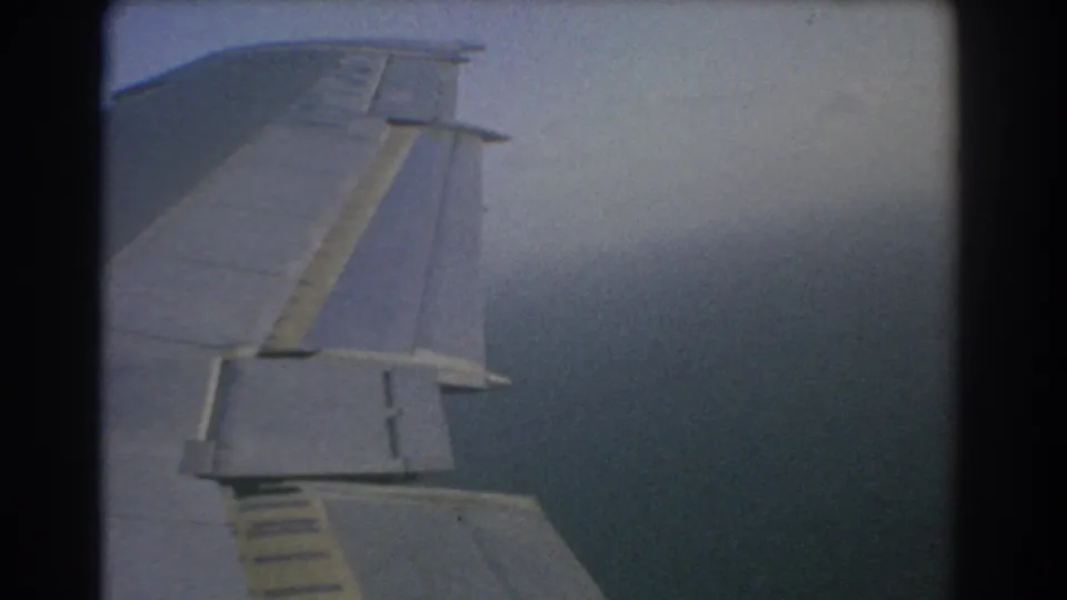 1967 Perth travel footage shows an airplane wing from a passenger window above a broad blue-gray sea.