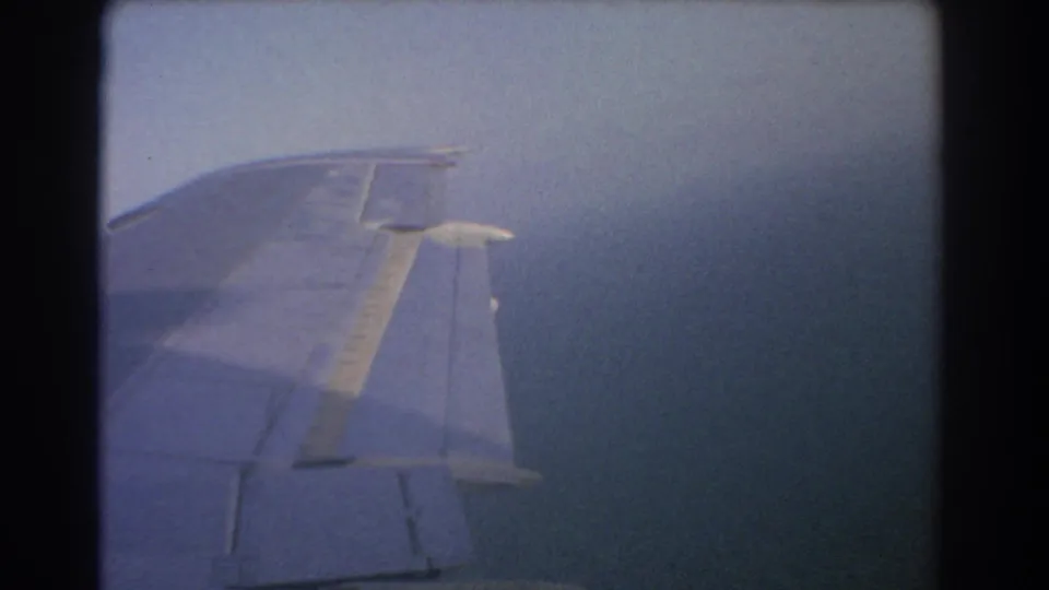 A closer 8mm passenger-window view of an airplane wing over the sea during 1967 Perth travel footage.