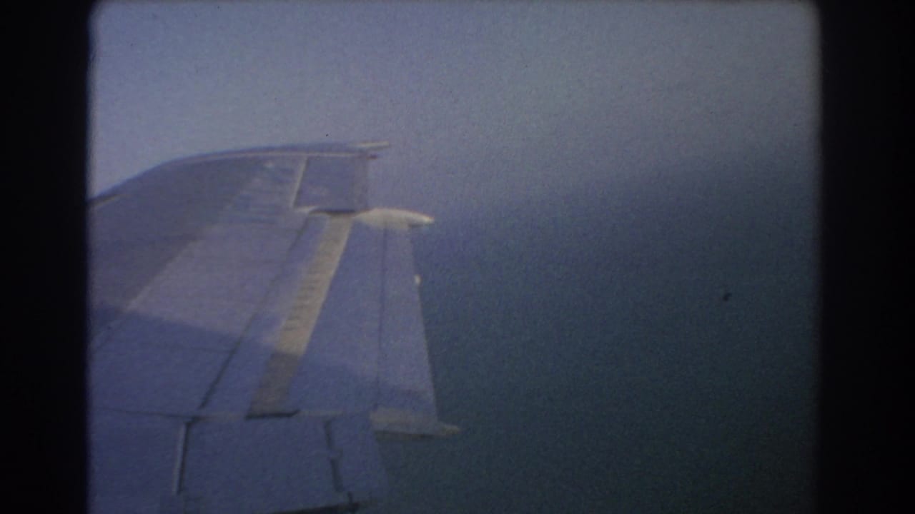 Airplane wing seen through a window above hazy water and sky.