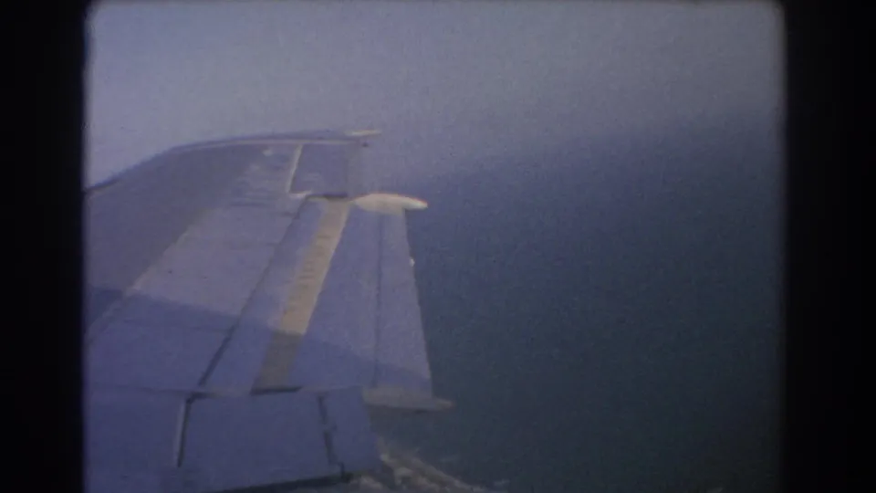 Airplane wing viewed from a passenger window during a 1967 8mm flight over water near Perth, Australia.