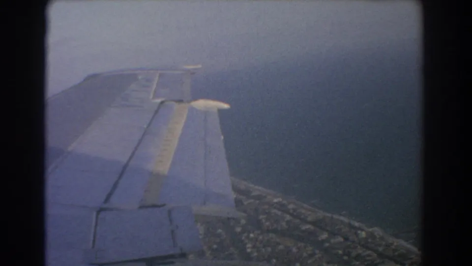 1967 8mm airplane-window view near Perth, Australia, showing the wing above water and a coastal strip below.