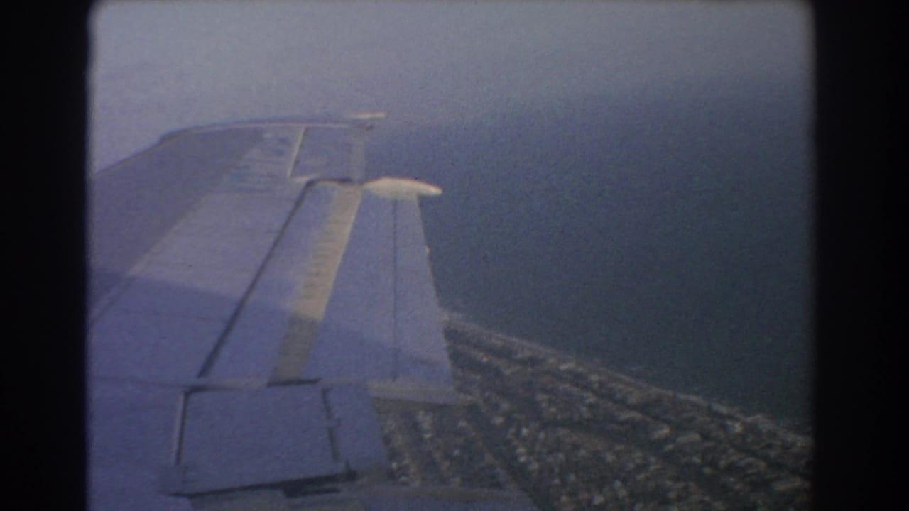 Airplane wing seen through a window above coastline and water.