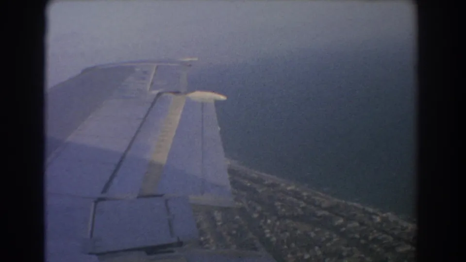 1967 8mm passenger view over Perth, Australia, with an airplane wing in the foreground and coastline below.