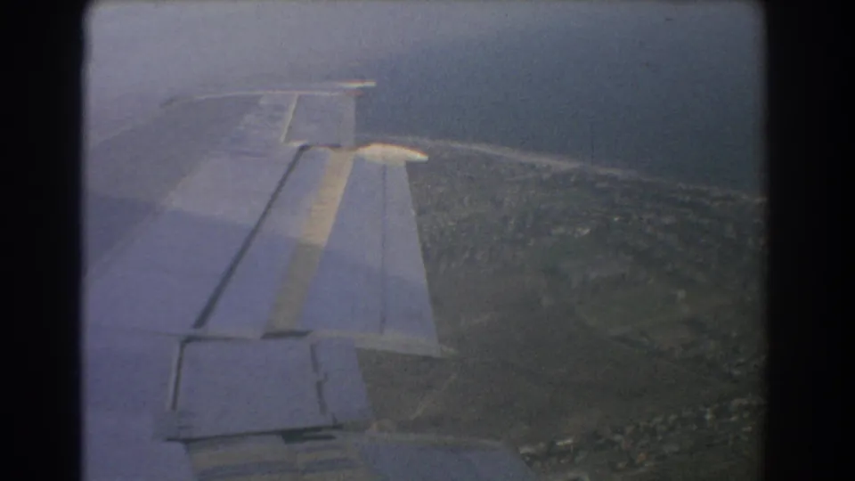 Passenger-window view from a plane over Perth, with the wing foregrounding coastal development and open land.