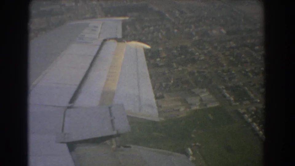 1967 8mm aerial frame near Perth showing a plane wing with flap detail over houses, roads, and open green land.
