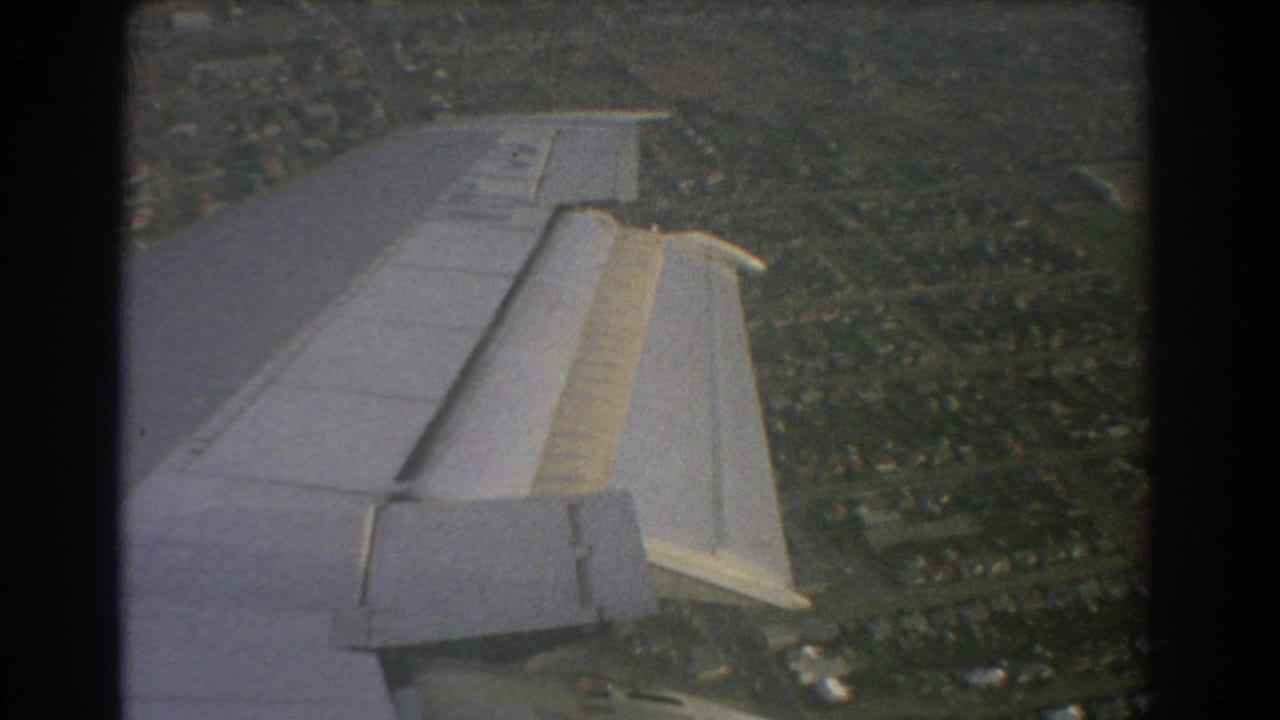 Aircraft wing seen from a passenger window above a suburban landscape.