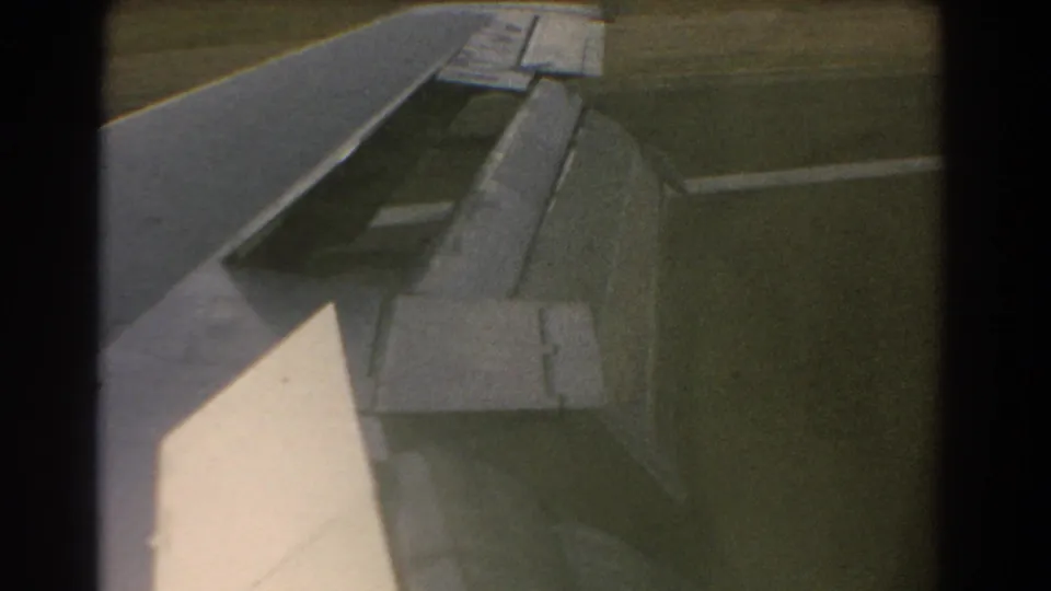 Passenger-window view of an aircraft wing and deployed flap near runway-side ground in the supplied 1967 Perth context.