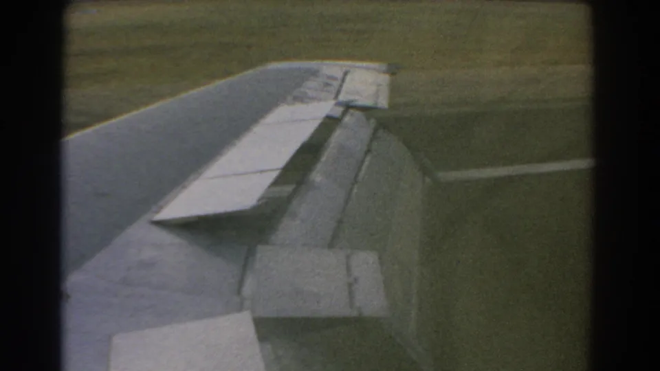 Passenger-seat view in 1967 Perth showing the aircraft wing, flap, and grassy runway area through the window.