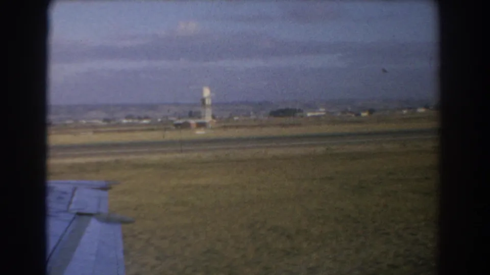 Final 1967 Perth airport frame showing the control tower, runway area, grass, distant horizon, and aircraft wing corner.