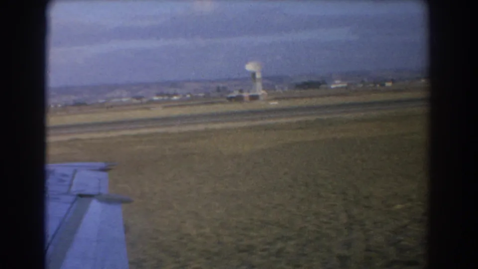 1967 Perth aircraft-window view with the wing in the foreground and a distant dish-like tower beyond the airfield.