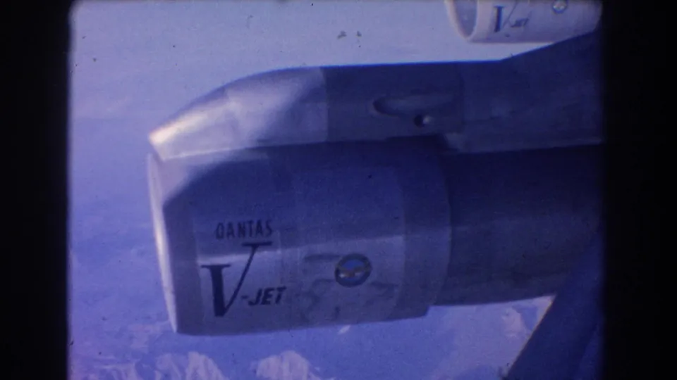 Blue-tinted 1967 aircraft-window view of a Qantas V-Jet engine with distant mountain peaks below.