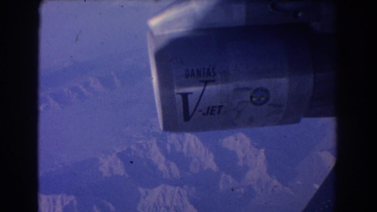 Qantas V-Jet engine seen through an airplane window above mountain peaks.