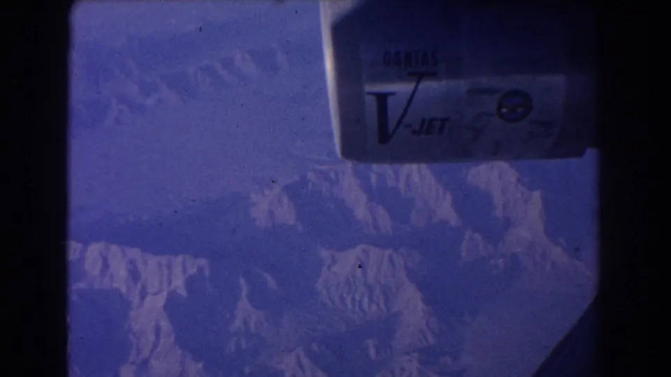 Qantas V-Jet branding appears on the engine as the airplane passes over snow-marked mountain terrain.