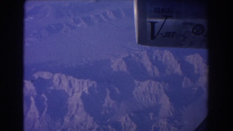Passenger-window view with part of the Qantas V-Jet engine at top right and rugged mountain peaks below.