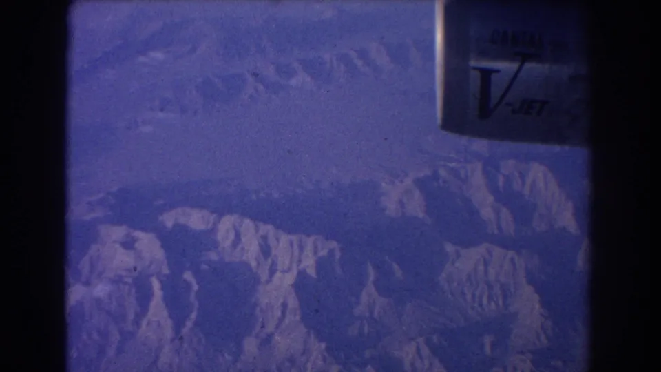 A blue-tinted 8mm view shows mountain ridges below and a partial Qantas V-Jet engine near the window edge.