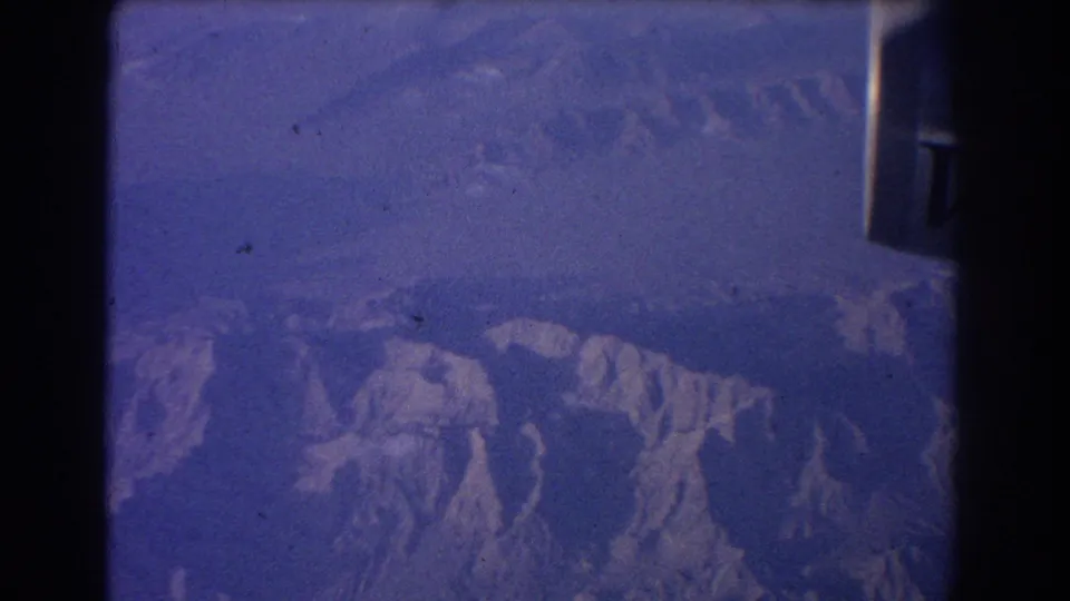 Blue 8mm aerial view over mountains with aircraft framing and a partial Qantas V-Jet mark near the upper edge.