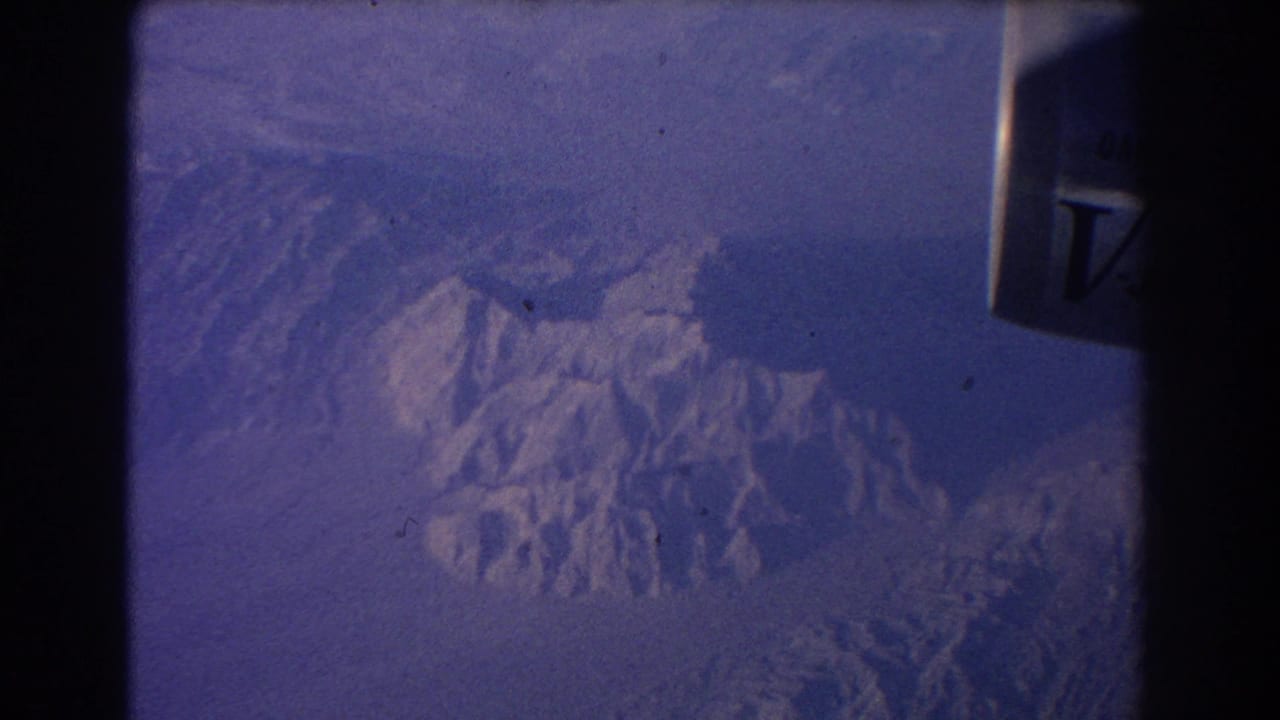 Jet engine edge and snowy mountain ridges seen through an airplane window.