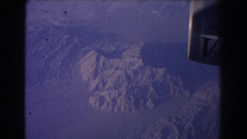 1967 8mm aerial view from a passenger window, with a jet engine marking at upper right and mountain ridges below.