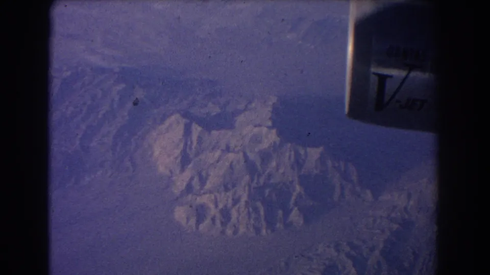 1967 8mm aerial passenger shot with the jet engine at right and hazy snow-dusted ridges below.