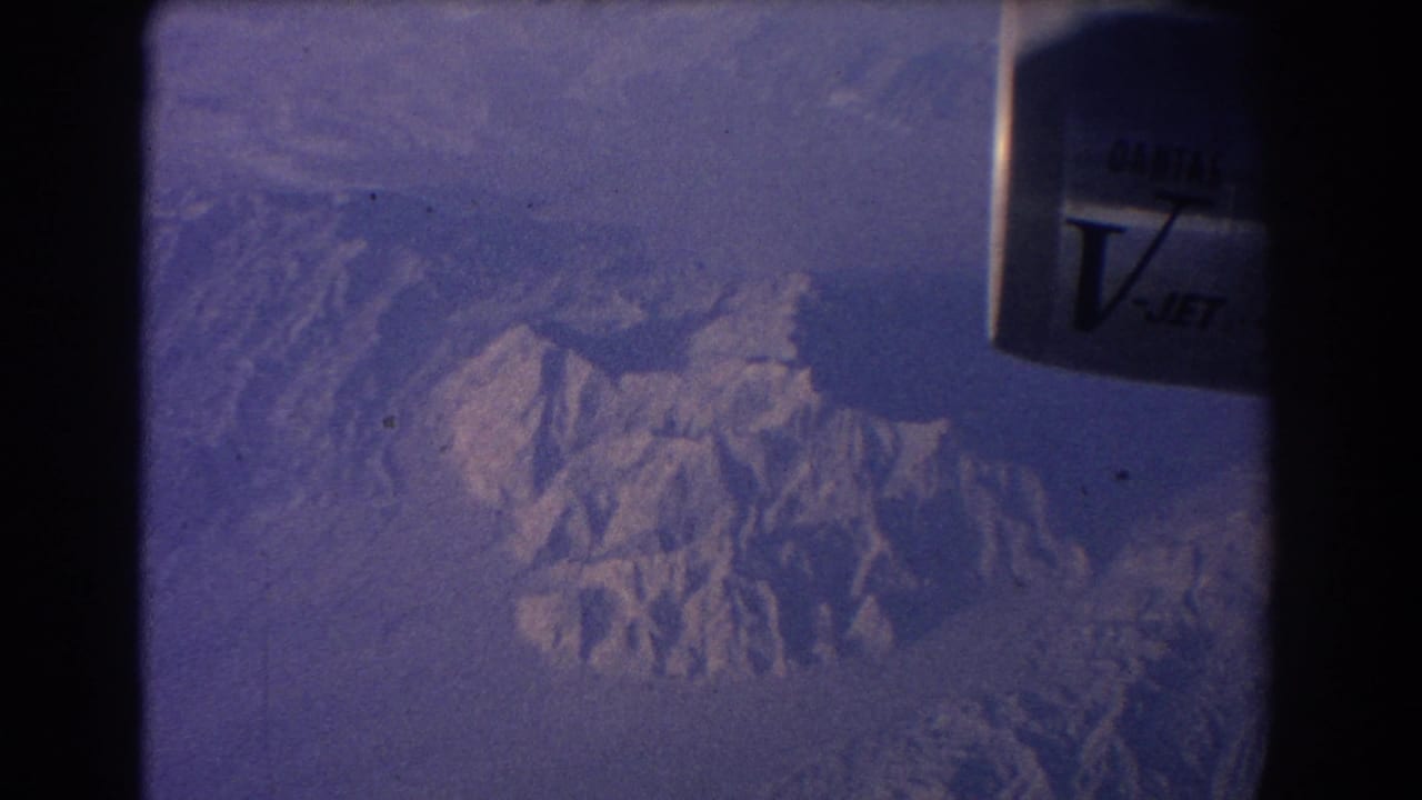 Snow-capped mountains seen through an aircraft window with Qantas V-Jet marking at the top right.