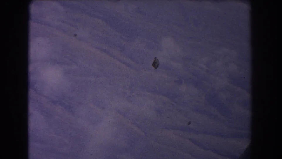 1967 8mm frame of textured mountain terrain near Sydney, Australia, with faded purple-blue color, grain, and small debris marks.