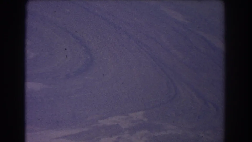 1967 8mm aerial landscape from Australia, showing soft terrain textures, pale bands, grain, and visible film wear.