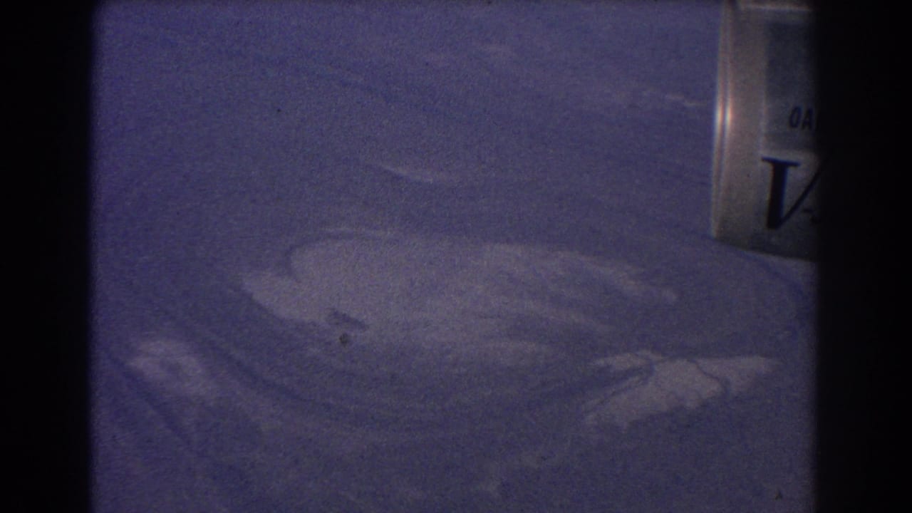 1967 8mm home-movie frame from the Sydney Australia clip showing ambiguous pale terrain or water patterns from above with a partial container edge.