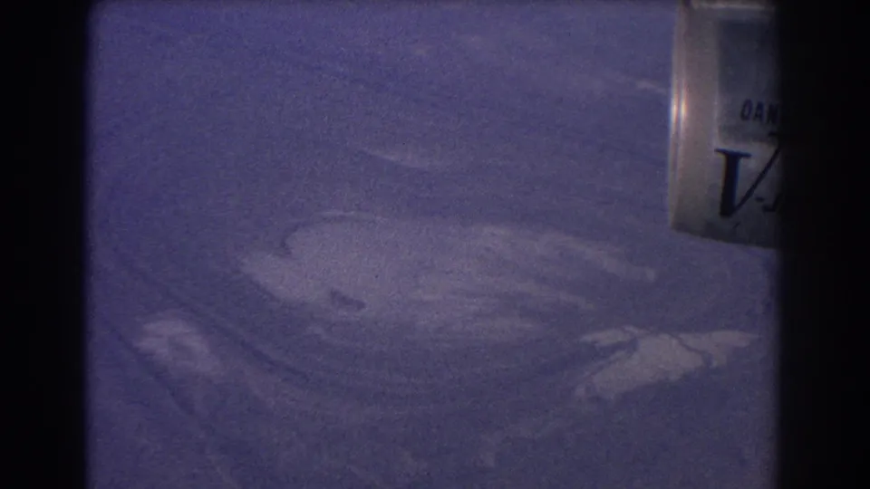 1967 8mm frame from the Sydney Australia clip showing abstract land or water patterns from above and a cropped container with partial lettering.