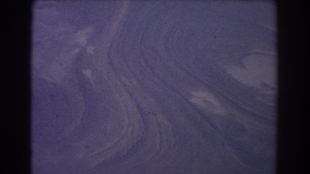 1967 8mm frame showing abstract purple ripples across dune-like terrain with grain and dark scan edges.