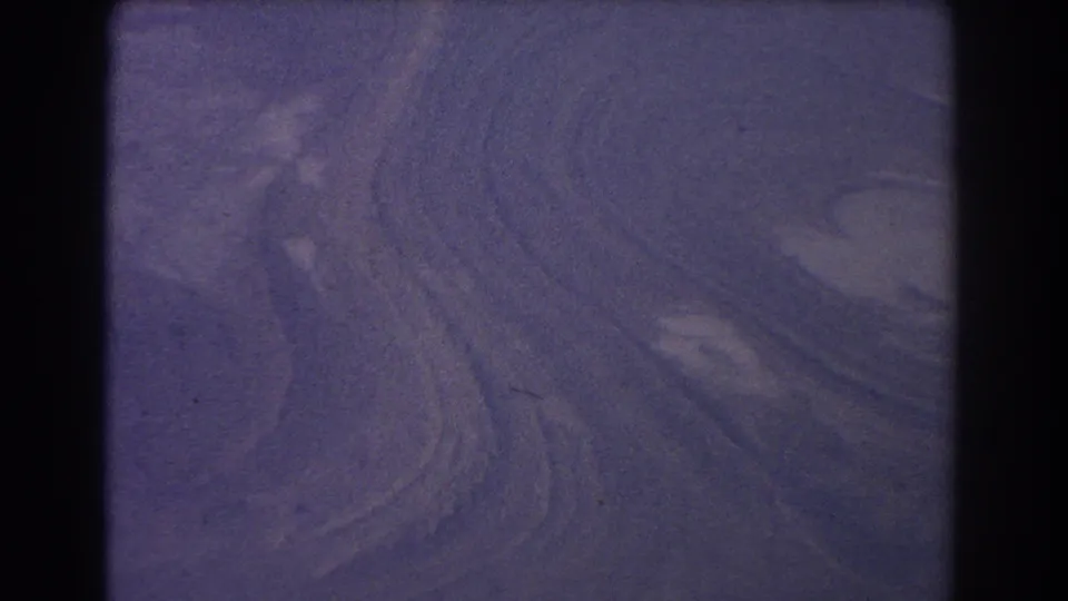 1967 8mm frame showing abstract purple ripples across dune-like terrain with grain and dark scan edges.