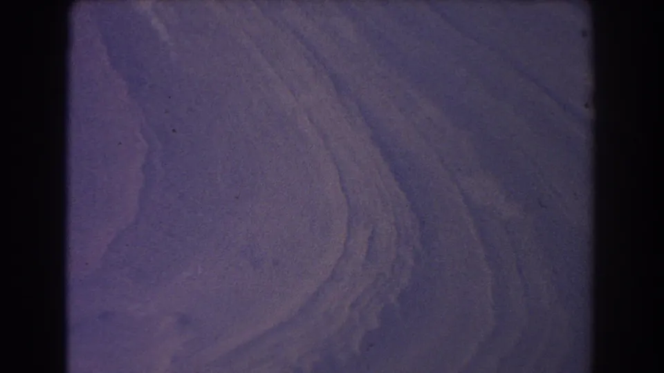 Abstract 8mm view of purple-blue dune-like curves, with visible grain and no identifiable landmark.