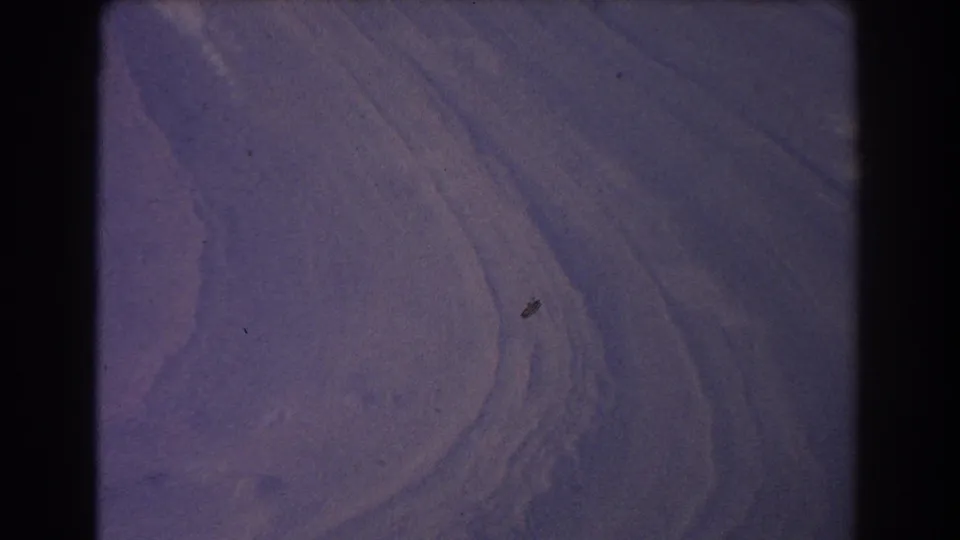 1967 archival frame with soft purple rippled terrain and a pale curve, scanned from 8mm film.