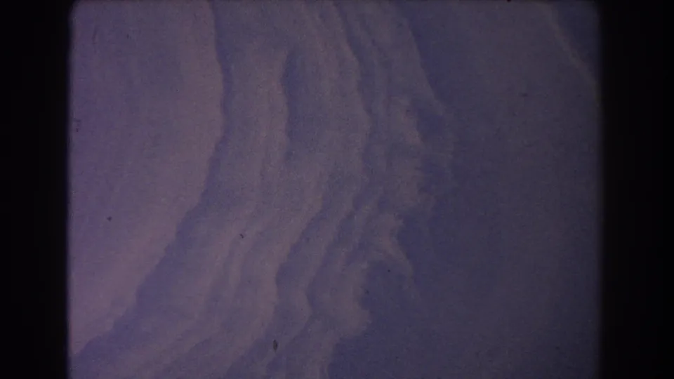 8mm frame of abstract purple dune-like terrain, with broad curves, grain, and no visible people or structures.