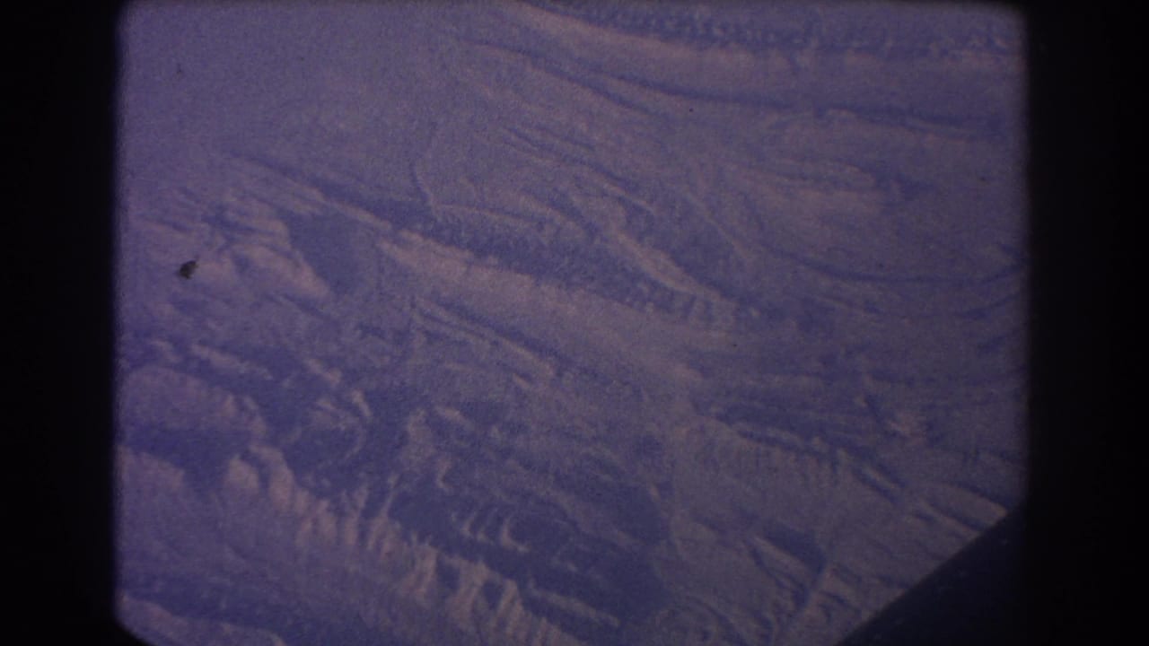 Snowy uneven terrain seen from above through dark film-frame edges.