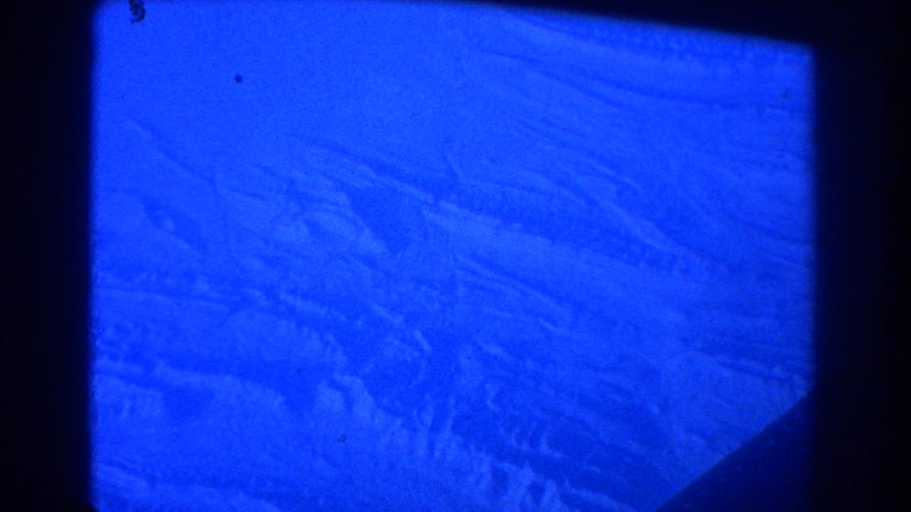 Blue-tinted aerial view through an airplane window with dark film-frame edges.