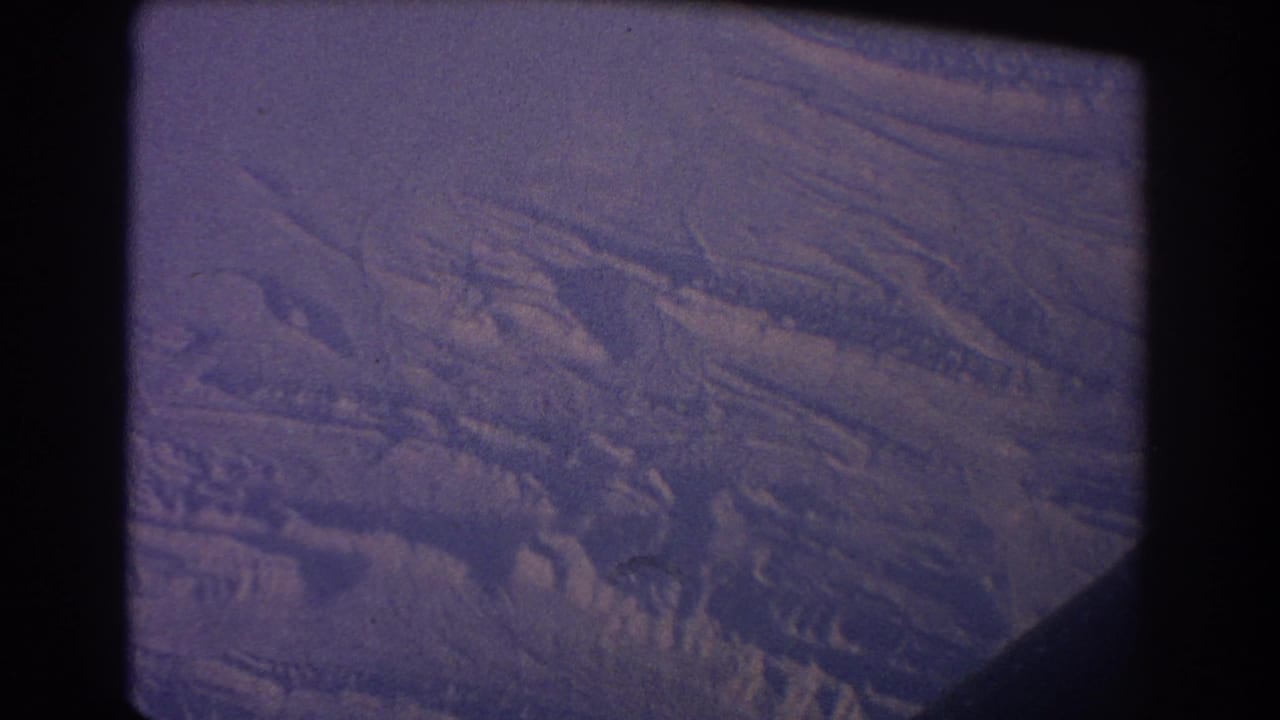 Violet aerial view of clouds and textured terrain through an airplane window.
