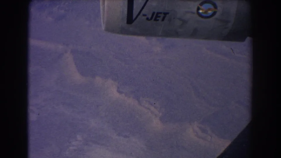 1967 8mm aerial view near Sydney, Australia, showing hazy grey-purple mountain terrain and a partial V-JET aircraft marking.