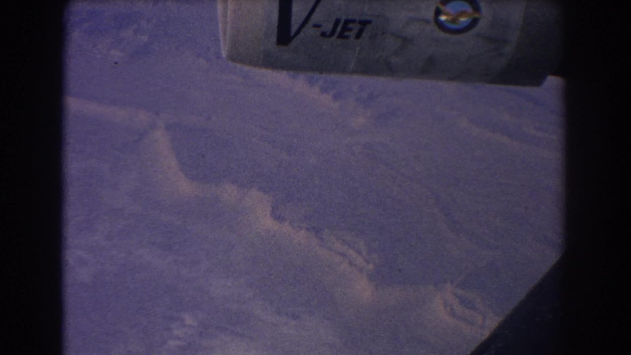 Mountain ridges seen from the air with a partial V-JET aircraft marking and dark window frame.