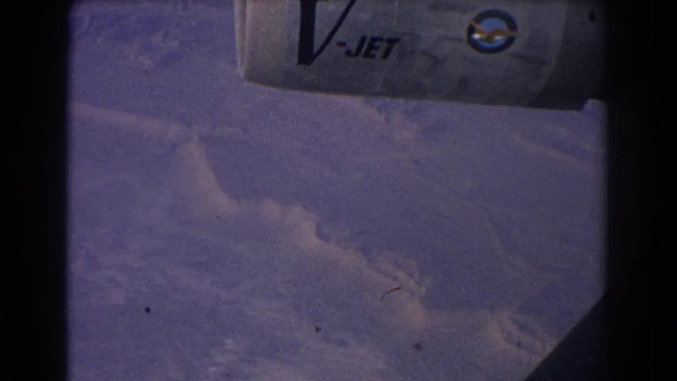 Faded 1967 8mm aerial view of rugged terrain below, with a partial V-JET aircraft marking visible at the top.