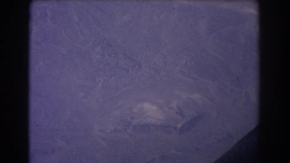 1967 8mm aircraft-window view near Sydney showing hazy mountain terrain, dark frame edges, and pronounced purple-grey fading.
