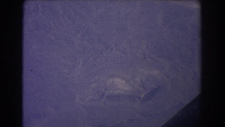 1967 Sydney-area 8mm frame showing a hazy aerial view of rugged coastal terrain with grain, scratches, and a dark edge in the lower right.